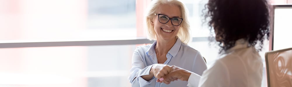 An experienced female chiropractor shakes hands with a younger associating chiropractor.