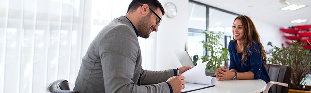 A hiring chiropractor reviews a woman's resume as they both sit at a desk.