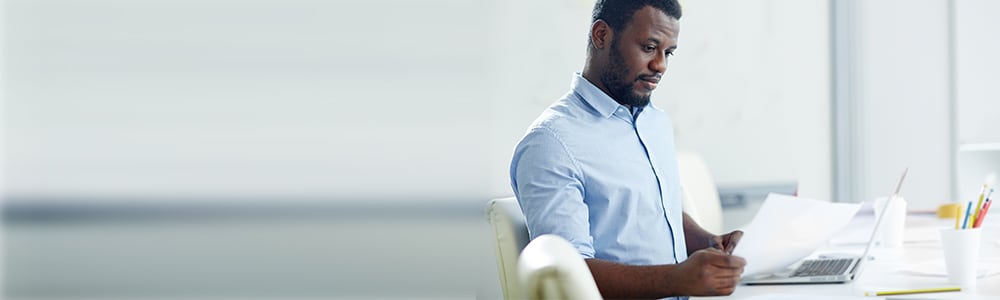 A man sits at his desk reviewing resumes.